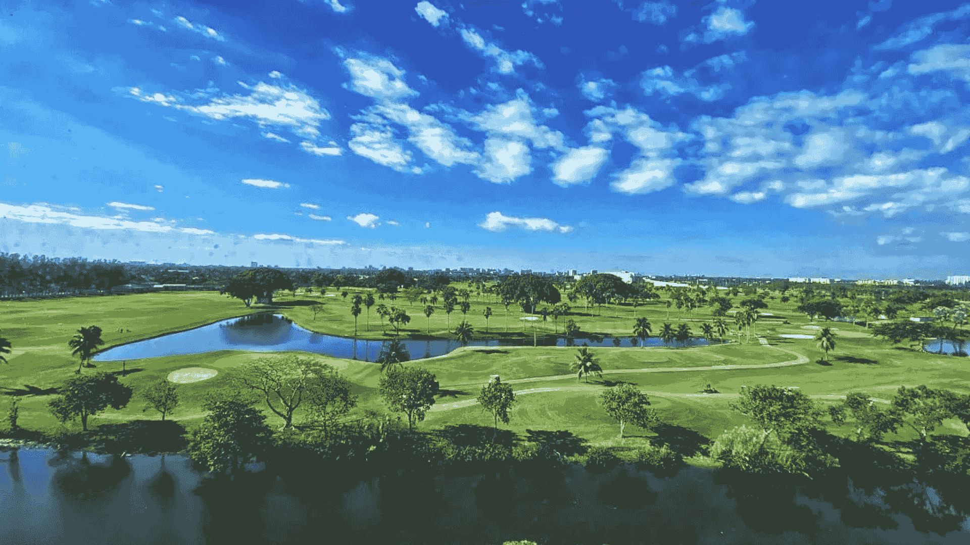 Aerial view of a Florida golf course with palm trees, lakes, and a city skyline on the horizon